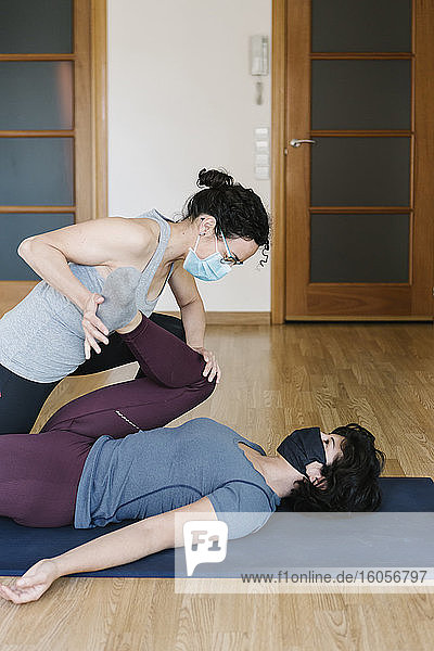 Physiotherapeutin mit Maske dehnt das Bein einer Patientin auf einer Übungsmatte im Club