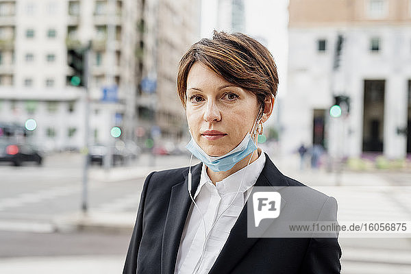 Nahaufnahme einer selbstbewussten Geschäftsfrau mit Maske vor einem Gebäude in der Stadt