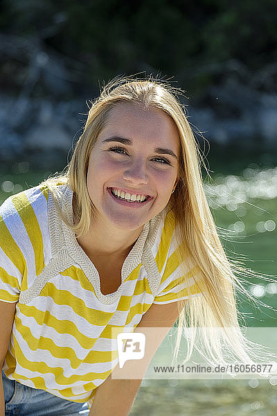 Lächelnde junge Frau mit blondem Haar steht am Fluss