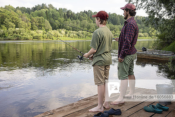 Vater und Sohn angeln im Fluss  während sie auf der Uferpromenade stehen