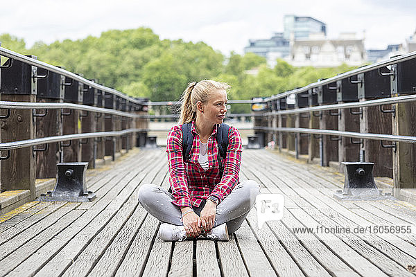 Mid adult woman wearing checked shirt looking away while sitting on bridge