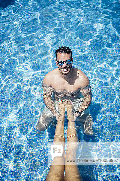 Mann mit Sonnenbrille hält Beine einer Frau im Schwimmbad
