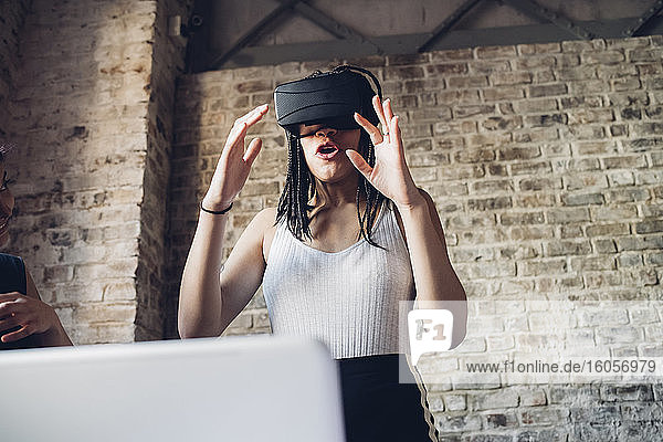 Excited young woman wearing Vr goggles in loft office