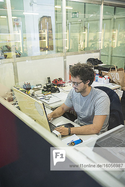 Junger Geschäftsmann  der einen Computer benutzt und in einem beleuchteten Büro sitzt