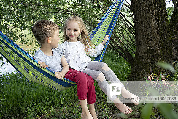 Mädchen im Gespräch mit einem Jungen  der in einer Hängematte im Wald sitzt
