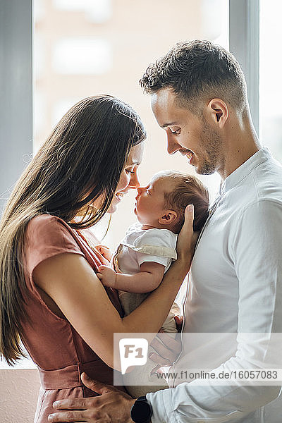 Happy parents playing with baby boy by window at home