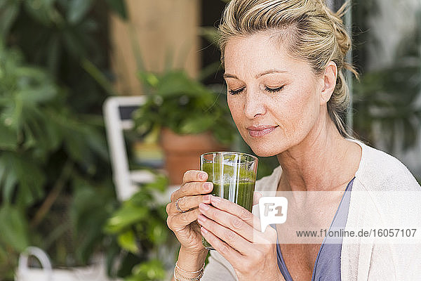 Portrait of mature woman with eyes closed with glass of green smoothie
