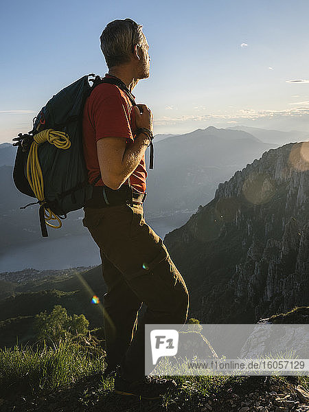 Männlicher Wanderer  der während des Sonnenuntergangs auf einem Berg stehend die Aussicht betrachtet  Orobie  Lecco  Italien