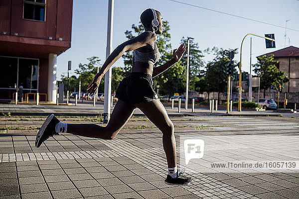 Female athlete listening music through headphones while running on street in city