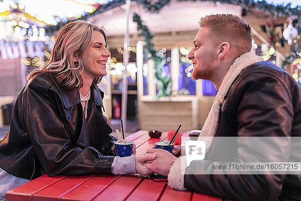 Romantisches Paar  das sich am Tisch die Hände hält  während es im Vergnügungspark sitzt