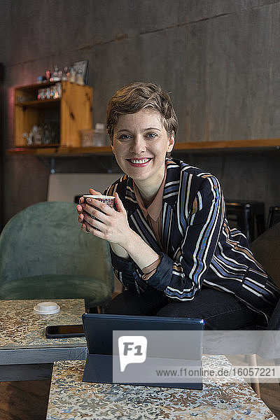 Porträt eines lächelnden Freiberuflers  der in einem Café mit digitalem Tablet und Smartphone sitzt