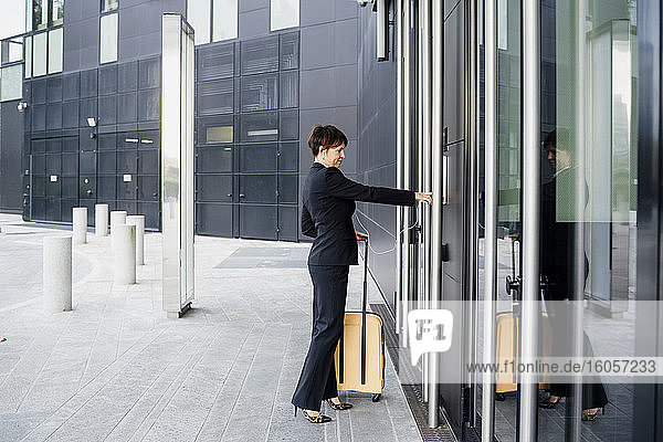 Geschäftsfrau mit Koffer beim Betreten eines modernen Gebäudes