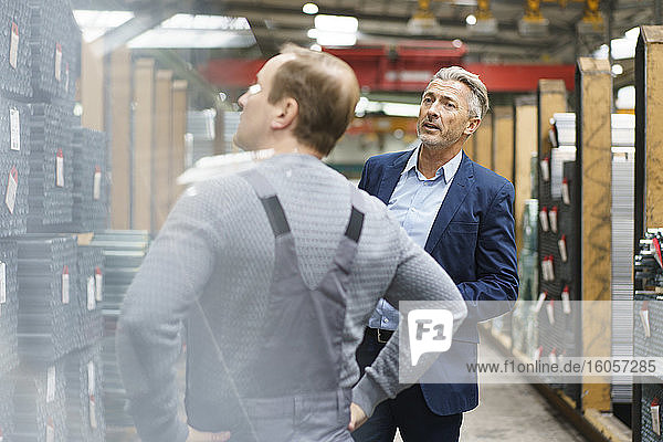 Geschäftsmann und Arbeiter unterhalten sich in einer Lagerhalle einer Fabrik