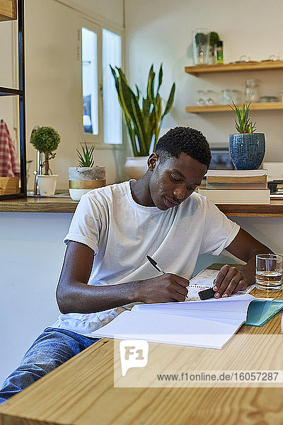 Junger Mann schreibt Notizen in ein Buch auf dem Tisch  während er zu Hause sitzt