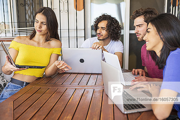 Junge Frau zeigt Laptop an multiethnische Freunde  die am Tisch im Hinterhof sitzen