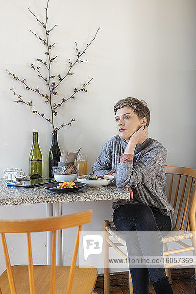 Nachdenkliche Kundin  die wegschaut  während sie mit einer Mahlzeit am Tisch in einer Cafeteria sitzt