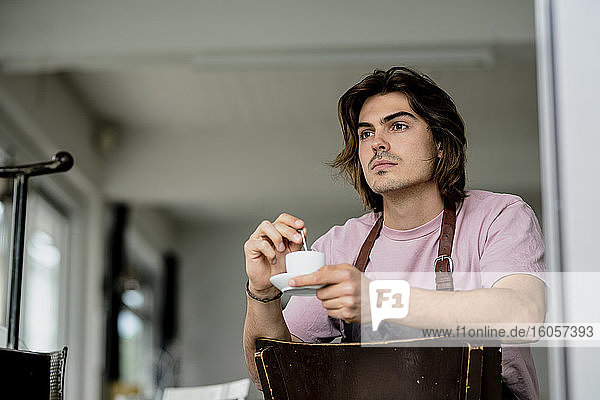 Nachdenklicher Besitzer hält Kaffeetasse  während er auf einem Stuhl im Café sitzt