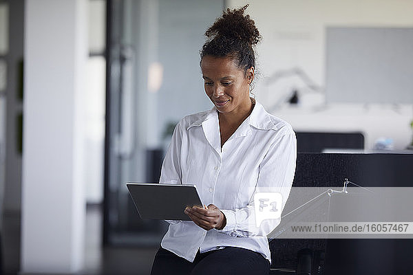 Porträt einer lächelnden Geschäftsfrau  die in einem modernen Büro ein digitales Tablet benutzt