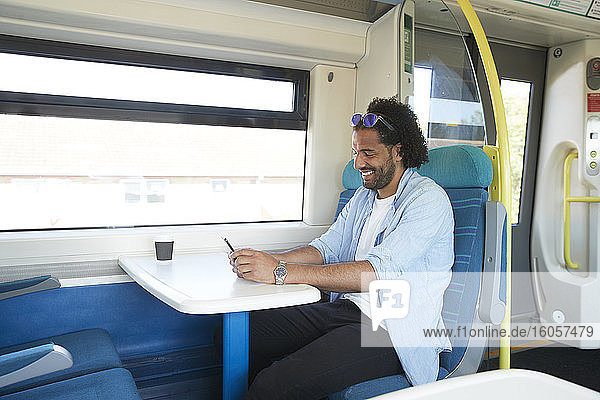Happy young trendy man using smart phone in train