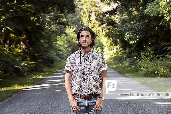 Nachdenklicher junger Mann steht auf der Straße inmitten von Bäumen im Wald