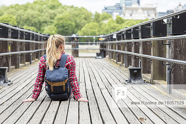 Mittlere erwachsene Frau mit Rucksack auf einer Brücke in der Stadt sitzend