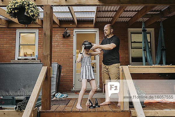 Vater trägt Virtual-Reality-Simulator zu Tochter  während er vor dem Haus steht