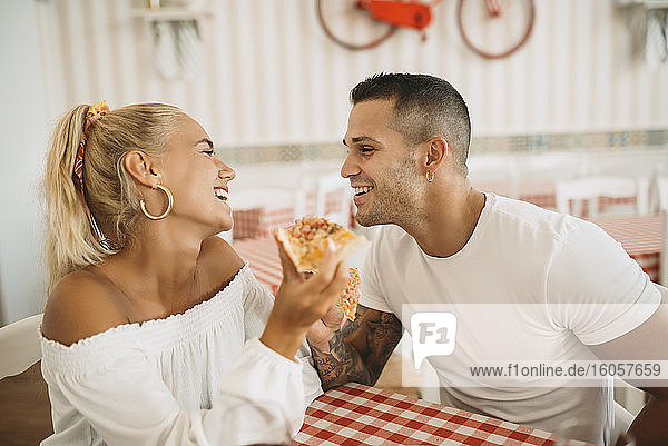 Happy young couple eating pizza while sitting in restaurant