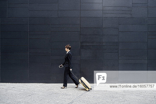 Geschäftsfrau mit Koffer zu Fuß auf dem Bürgersteig von modernen Gebäude in der Stadt