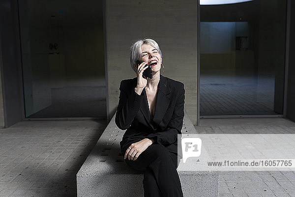 Fröhliche Geschäftsfrau  die über ein Smartphone spricht  während sie im Büro sitzt