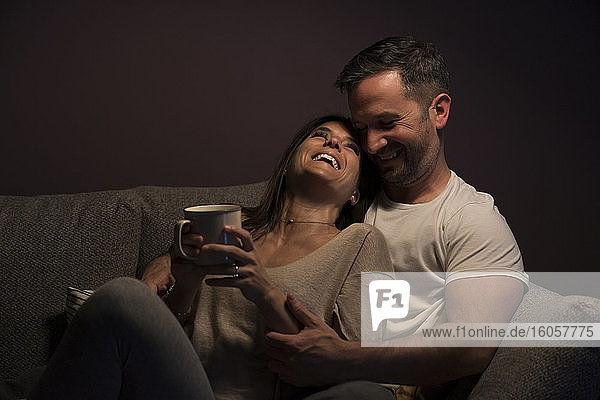 Verliebtes Paar lacht beim Entspannen auf dem Sofa an der Wand zu Hause