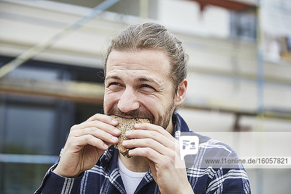 Porträt eines Arbeiters in der Mittagspause auf einer Baustelle  der ein Brot isst