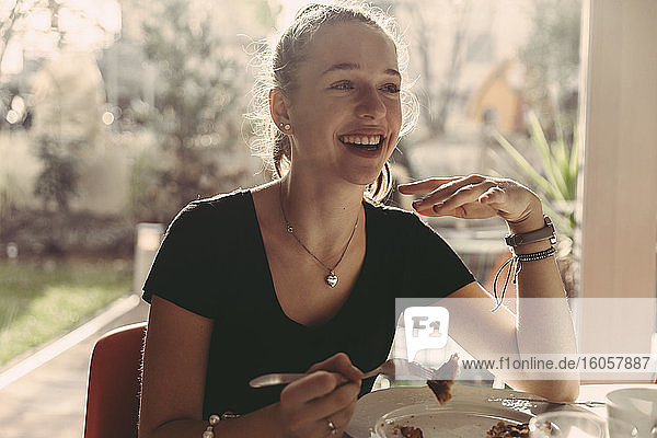 Glückliches Mädchen im Teenageralter genießt das Frühstück  während sie zu Hause wegschaut