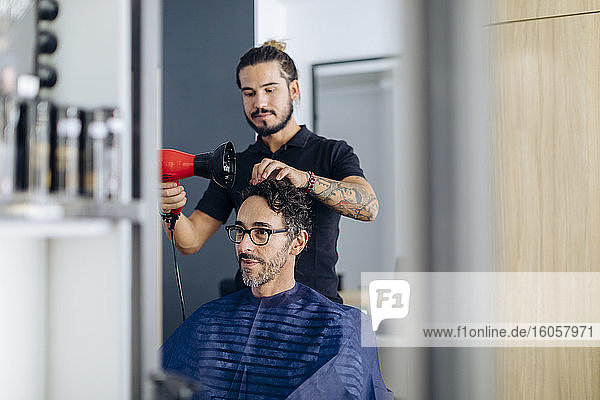 Friseur föhnt die Haare eines Mannes im Salon