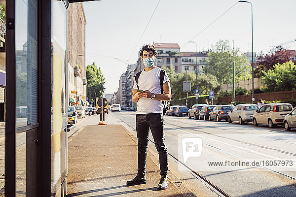 Junger Mann mit Maske  der wegschaut  während er auf der Straße in der Stadt steht