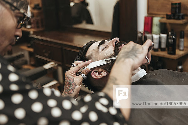 Trendy Barbier schneidet Bart eines Mannes im Salon