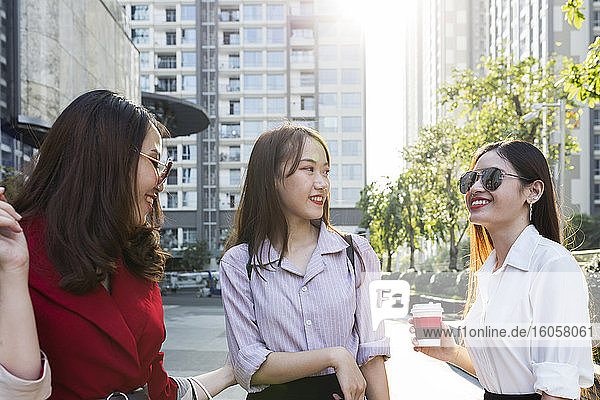 Female friends talking while standing against buildings in city