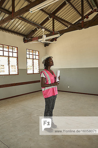 Female architect holding blueprint standing in school building at construction site