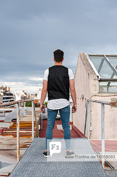 Young man standing on abandoned terrace against cloudy sky