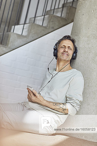 Älterer Mann mit Kopfhörern  der in einer Loftwohnung Musik hört