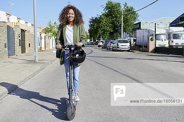 Glückliche Frau fährt elektrischen Roller auf der Straße an einem sonnigen Tag