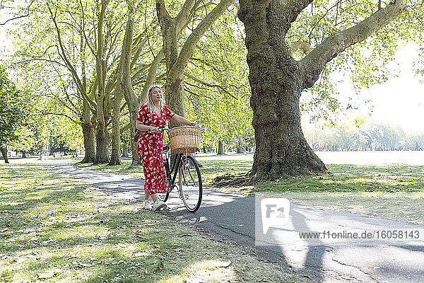 Thoughtful woman walking with bicycle on footpath in public park