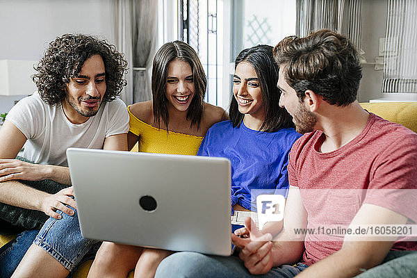 Lächelnde multiethnische Freunde teilen sich einen Laptop  während sie im Wohnzimmer sitzen