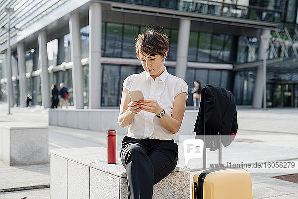 Weibliche Fachkraft  die ihr Smartphone benutzt  während sie auf einem Sitz in der Stadt sitzt