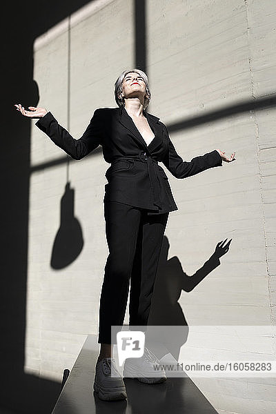Weibliche Fachkraft in stilvollem Anzug steht auf Stützmauer mit Sonnenlicht und Schatten im Hintergrund