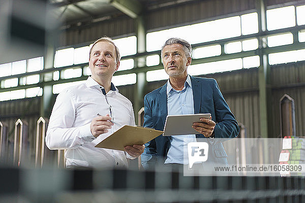 Two businessmen with tablet and clipboard having a meeting in a factory