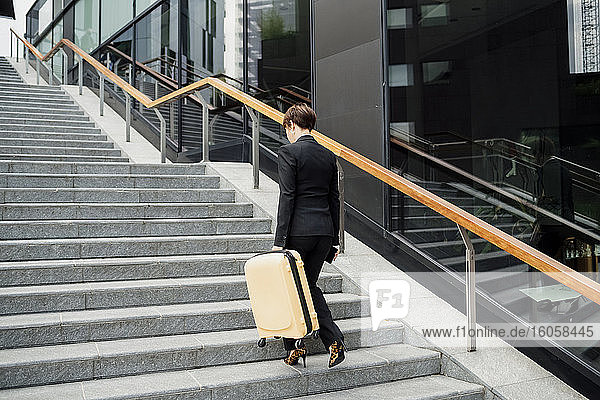 Businesswoman with suitcase walking on steps in city