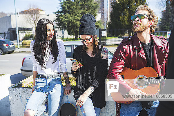Bearded man playing guitar while standing with female friends in city