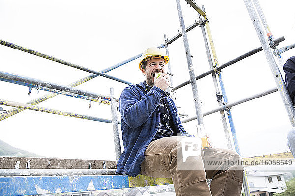 Bauarbeiter isst Essen  während er auf der Baustelle gegen den klaren Himmel sitzt