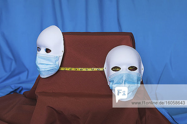Studioaufnahme von zwei Theatermasken  die Schutzmasken tragen  getrennt durch ein Maßband
