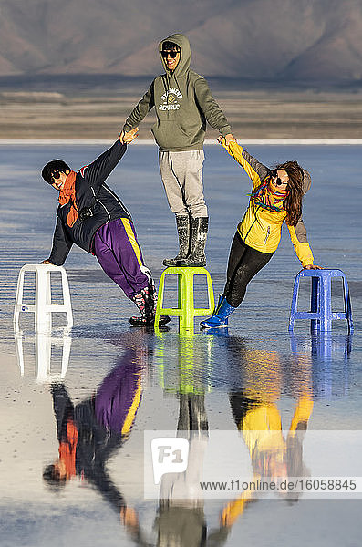 Touristen posieren in der Reflexion während der Regenzeit (Dezember-Februar) im Salar de Uyuni  der größten Salzfläche der Welt; Abteilung Potosi  Bolivien